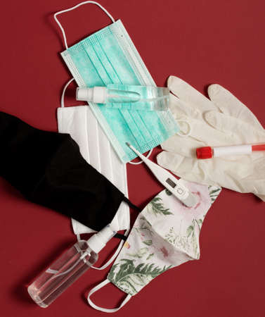 Surgical masks, cotton reusable masks and hand sanitizers, thermometer and blood medical test on red...