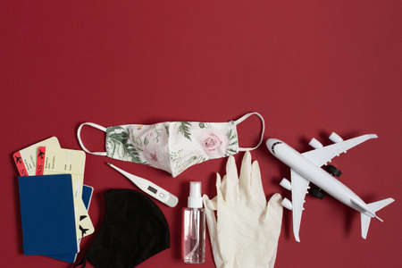 Safe travel during virus. Passport and boarding pass with surgical mask, alcohol antiseptic gel and thermometer on dark red background top view. Protectiv accessories from virus during traveling.の写真素材