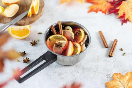 Hot mulled wine with citrus, apples, cinnamon sticks, and anise stars in cooking pan on grey table background in autumn time.の写真素材