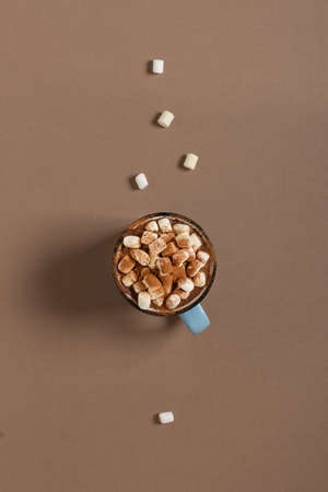 Hot chocolate with marshmallows and cinnamon spice in enamel mug on brown background top view. Vertical orientation and minimalism conceptの写真素材