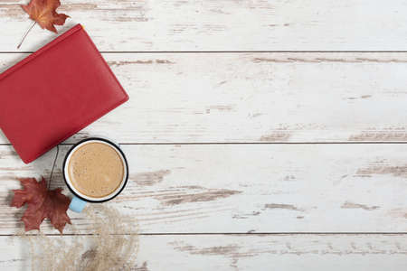 Cup of coffee, book and autumn colorful leaves on white wooden background top view. Autumn...