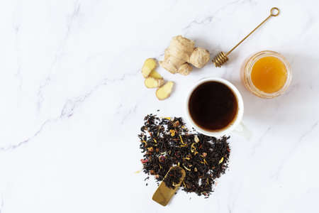 Cup of black tea with dinger and honey top view on white marble background. Healthy eating,...