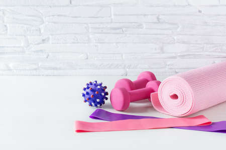 Dumbbells, fitness rubber bands, yoga mat and massage ball on white floor over white brick wall. Fitness equipment.の写真素材