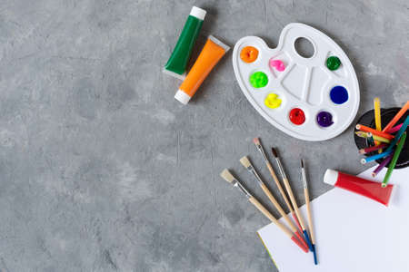 Pain brushes, watercolours and paint palette top view with blank sketchbook on grey concrete background. Creativity and hobby concept.の写真素材