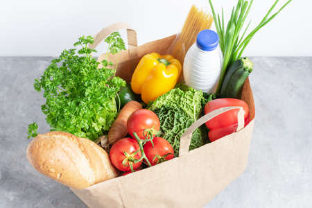 Paper shopping box full of fresh organic vegetables and grocery products on grey table. Eco-shopping or food delivery concept.の写真素材