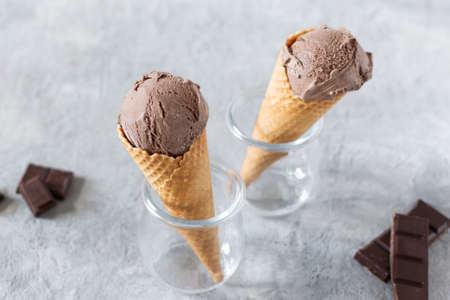 Balls of chocolate ice cream in a waffle cones in a glass jar on grey background. Refreshing summer...