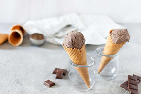 Balls of chocolate ice cream in a waffle cones in a glass jar on grey background. Refreshing summer dessert.の写真素材