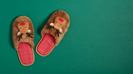 Cozy Christmas slippers on modern green background top view. Christmas celebration at home.