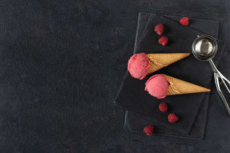 Raspberry ice cream in a waffle cones on black table top view. Summer refreshing sorbet.