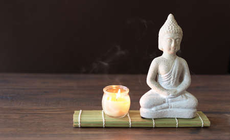 Buddha figure in meditation with burning candle on brown  background. Relaxation balance concept.の写真素材