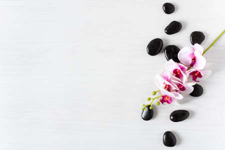 Black spa stones with orchid flower top view on white wooden background. Meditation stone background. Relaxation spa treatment concept.の写真素材