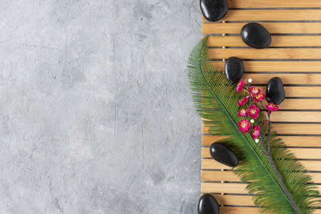 Black spa stones with flowers and palm leaf top view on grey concrete background. Meditation stone background. Relaxation spa treatment concept.の写真素材
