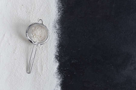 Sifted wheat flour over black surface with sieve top view. Food background.の写真素材
