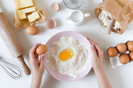 Preparing dough for baking top view on white table with ingredients and tools. Flour with egg in a bowl.の写真素材