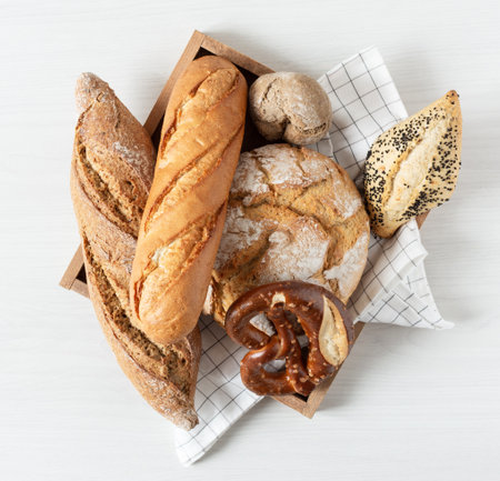 Assortment of baked bread and buns in a wooden box on white wooden background top view. Healthy...