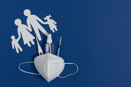 Paper cut silhouette of a family and medical protective mask with thermometer, hand sanitizer and syringe with vaccine top view on blue background. Concept of virus protection for all family.の写真素材