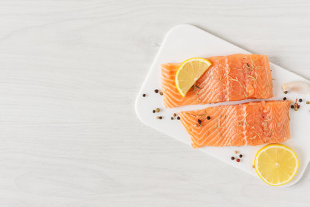 Fresh uncooked salmon fish fillet with paper spice and slices of lemon on white wooden background top view. Healthy eating full of omega 3.の写真素材