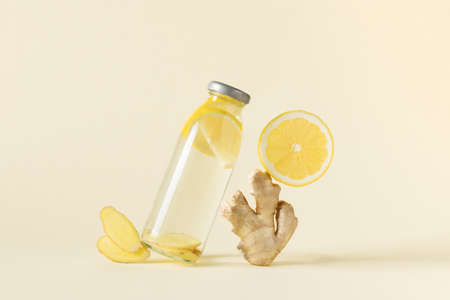 Bottle of infused water with ginger and lemon over light yellow background. Balanced still life of...