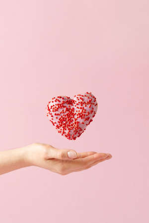 Heart shaped donut and women hand over pastel pink background. Creative baking for st. Valentine's...