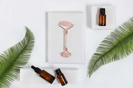 Pink quarts face massage jade roller with cosmetic massage oil on white background top view. Face...