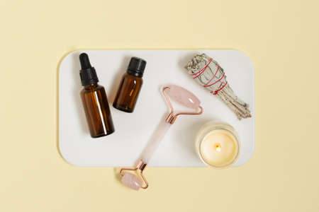 Pink quarts face massage jade roller with cosmetic oil and white salvia for relaxing on yellow background top view. Face care treatment.の写真素材