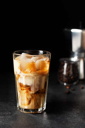 Iced coffee in a tall glass on black background. Cold refreshment summer drink.
