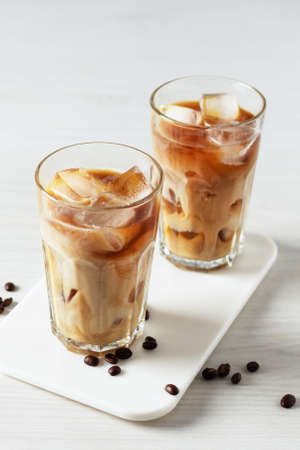 Iced coffee in a tall glass on white wooden table. Cold refreshment summer drink.