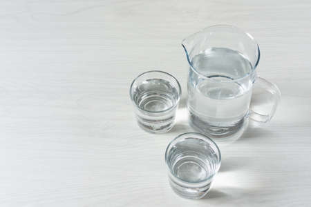 Two glasses and a jug with water on white wooden background. Refreshment drinking water, dieting and health care beverage.の写真素材