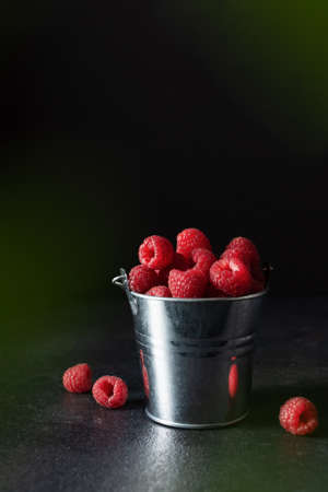 Fresh ripe raspberries in a metal small bucket on black background. Juicy raspberry full of vitamins.の写真素材