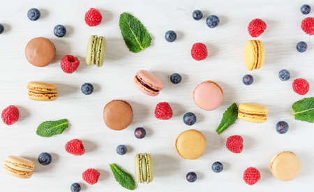 Background of multi colored french macaroons and berries such as raspberry and blueberry and mint leaves top view. French meringue cookie macarons and berries wallpaperの写真素材