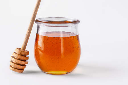 Honey in a glass jar and wooden honey dipper on white background. Honey, as a healthy sweet dessert.の写真素材