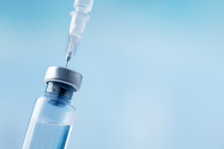 Glass vial and syringe with injection over blue background. Vaccination or beauty therapy concept.