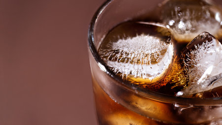 A glass of cola drink with ice cubes. Fresh cold sweet cola drink with ice one brown background with copy space.の写真素材