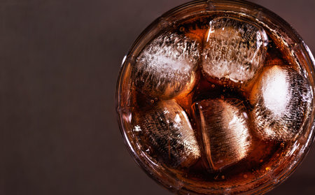 A glass of cola drink with ice cubes top view. Fresh cold sweet cola drink with ice on brown background with copy space.の写真素材