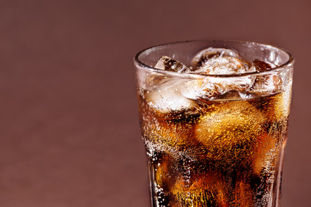 A glass of cola drink with ice cubes. Fresh cold sweet cola drink with ice on brown background with copy space.の写真素材