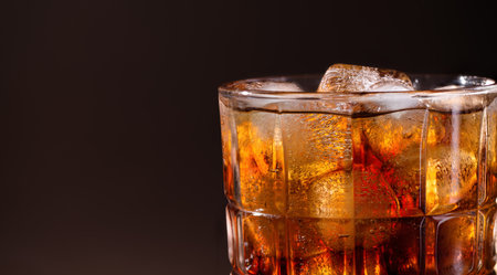 A glass of cola drink with ice cubes. Fresh cold sweet cola drink with ice on brown background with copy space.の写真素材