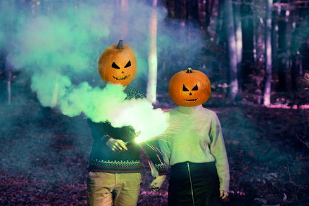 A couple with Halloween pumpkin on head in a woodland night with colourful smoke. Halloween...