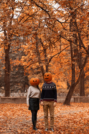 A couple with Halloween pumpkin on head in autumn woodland. Halloween Jack-o-lantern funny party.の写真素材
