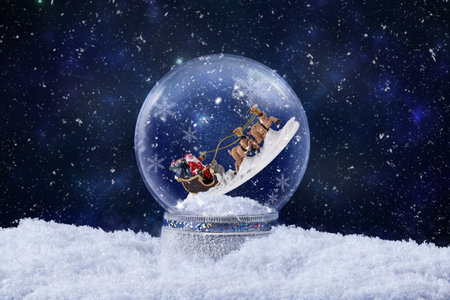 Christmas snow globe with Santa Claus ride on reindeer inside. Christmas greeting card with magic snow globe decoration with snow falling. Christmas background.の写真素材