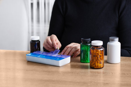 Female putting prescription pills and vitamins in a daily pill box organizer. Sorting nutritional supplements and antibiotics into weekly pills container.の写真素材