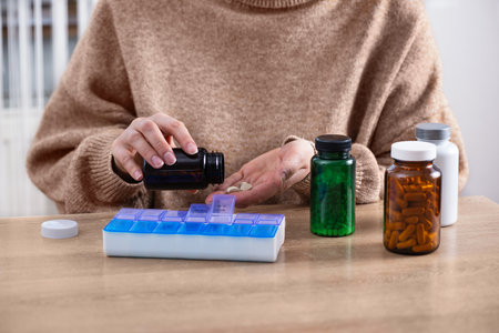 Female putting prescription pills and vitamins in a daily pill box organizer. Sorting nutritional supplements and antibiotics into weekly pills container.の写真素材
