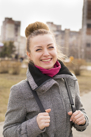 Portrait of pretty fashion blondie european woman looking at camera. Student or young enterpreneur with black backpack is walking on the park in early spring. Shining smile.の写真素材