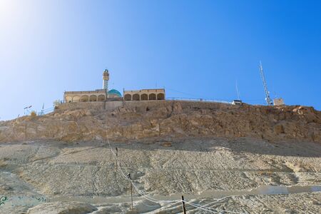 A mosque with a minaret and a blue dome on top of a rocky mountain in the desert against a blue sky. Prophet Khidr or Khezr Temple in city of Qom, Iranの写真素材
