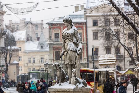 Lviv, Ukraine, January 05.2016: The view of a winter city with trams, lanterns and Christmas decorations and the sculpture of the goddess Diana strewn with snow on the foreground on the Market Squareのeditorial素材
