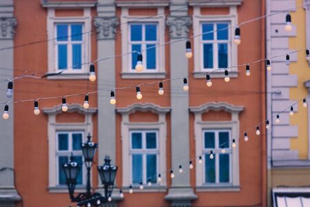 Garlands with bulbs on the background of blue windows of buildings and a street lamp in the center of a European city. Christmas fabulous atmosphere on Market Square in Lviv, Ukraineの写真素材