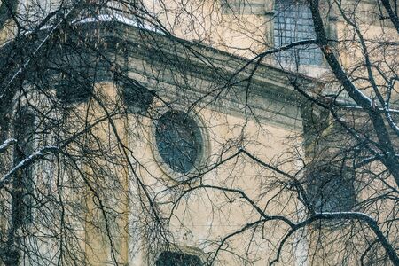 Wall and round stained glass window of the Dominican church and monastery in Lviv, Ukraine framed by bare tree branches. Winter city background. Snow covered branchesの写真素材