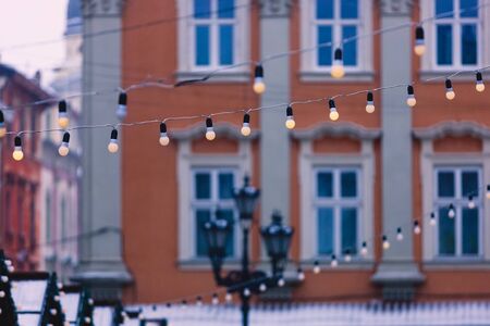 Garlands with bulbs on the background of blue windows of buildings and a street lamp in the center...