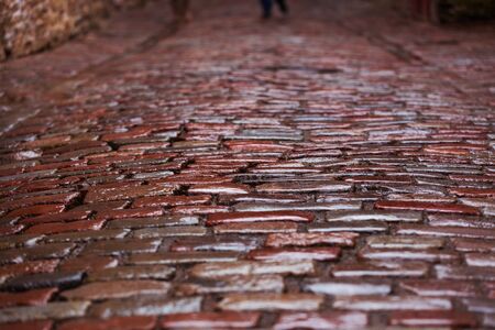 Paving with granite stone close-up with feet on the background. Red wet stones in rainy weather....