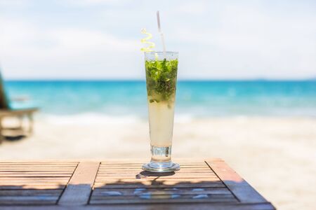 Refreshing tropical cocktail. Drink on the beach. Green and yellow cocktail in cool glass with straw on a table at the paradise ocean beach. Free space for textの写真素材