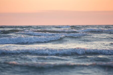 Seascape. Atmospheric image of sea waves. Beautiful sunset. White horses sea waves at soft orange...